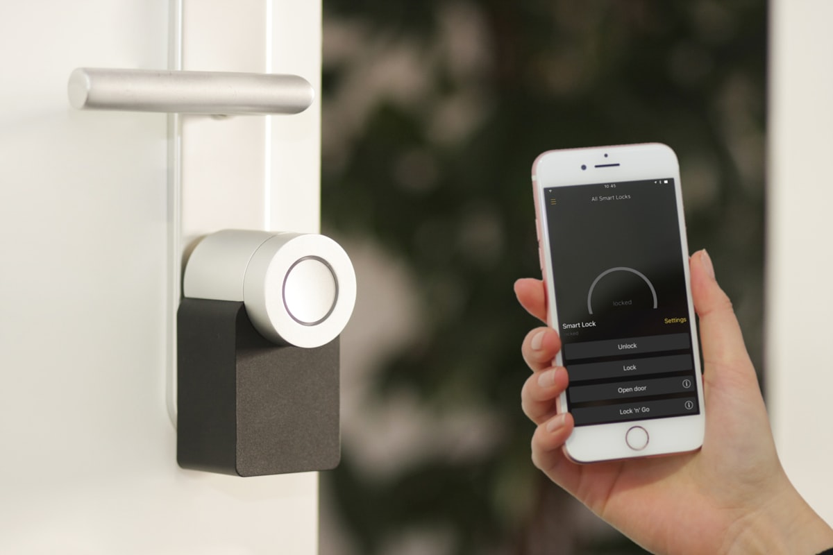 A hand held flat against an electronic door reader mounted beside an apartment entry, the reader's small indicator light just visible.